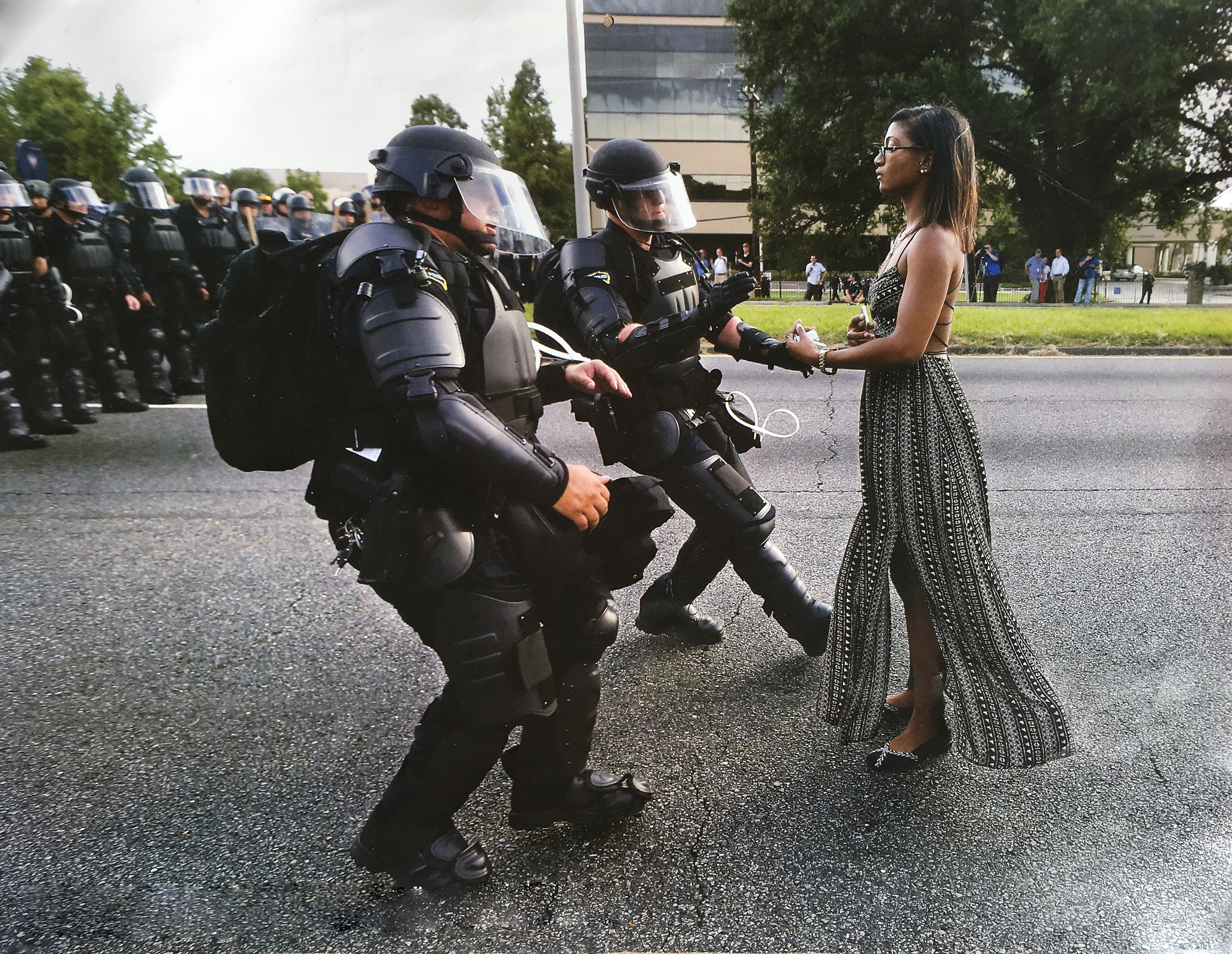 Police in riot gear detaining woman in flowing black and white dress